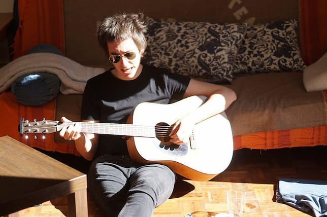 Alberto toca la guitarra, sentado en el suelo