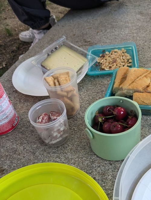 En la pared de un parque hay varios platos repartidos en latas de Tupperware: queso, cerezas, patatas fritas y bocadillos. Cerezas, patatas fritas y bocadillos